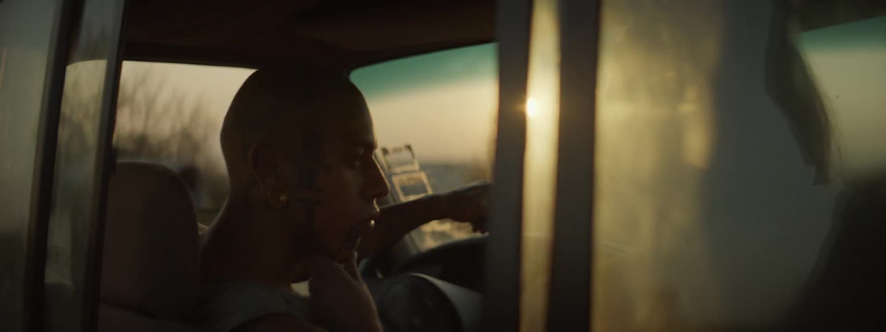 A young woman sits inside a pickup truck with a tattooed male and caresses his face as they look at each other