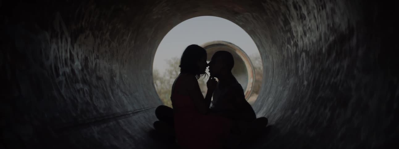 Silhouette of romantic couple sitting in a concrete pipe kissing