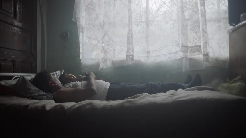 Father and son resting on a bed in a dim lit bedroom