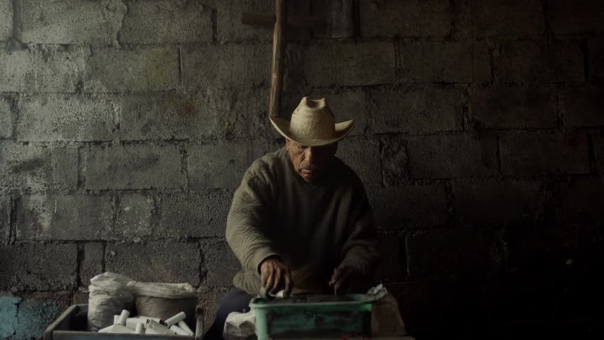 An elderly hispanic male hammers on a tool as he packs more dirt into a small tube