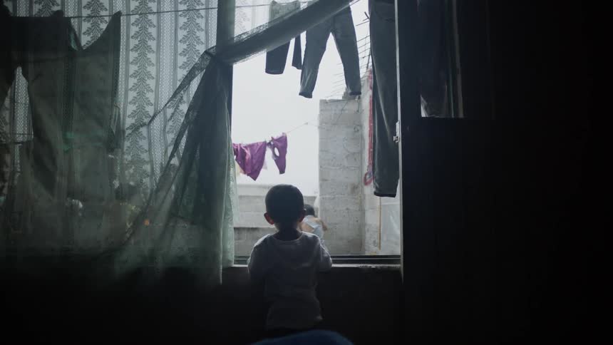 Kids play outside while a child stares out a window from inside