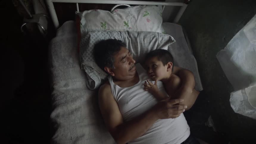 A man lays in bed holding a young boy in his arm