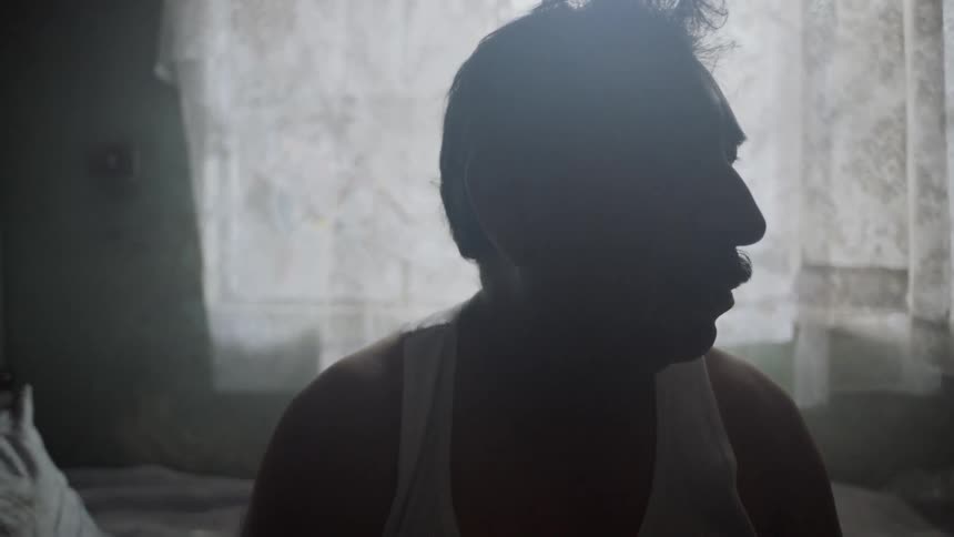 A man sits on his bed and looks off in to the distance