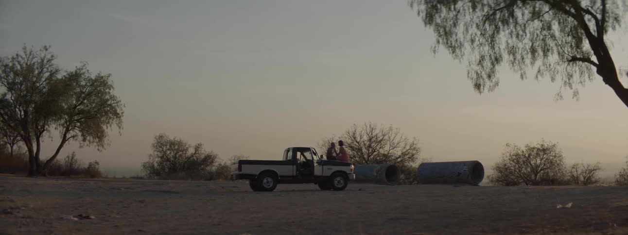 A pickup truck with the door open with a man and a woman sitting in the background kissing