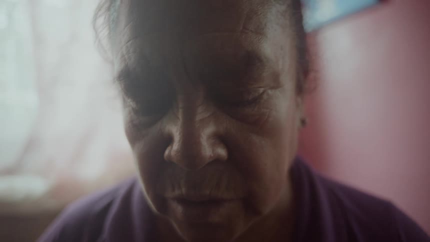 An elderly woman reading something as she stands in a house