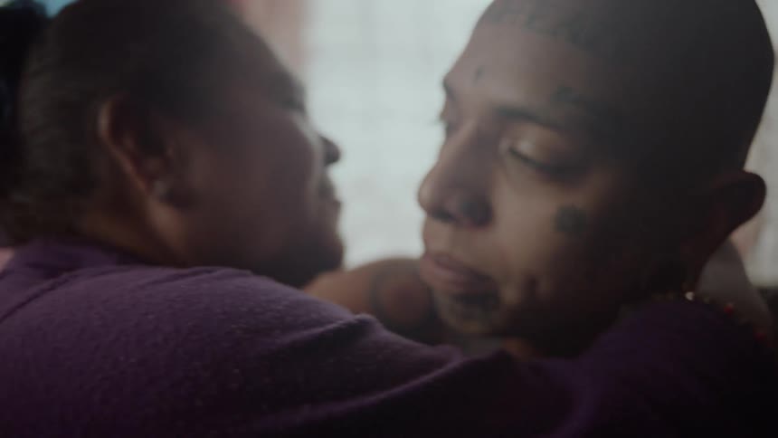 Old woman hugging and blessing a tattooed latino man