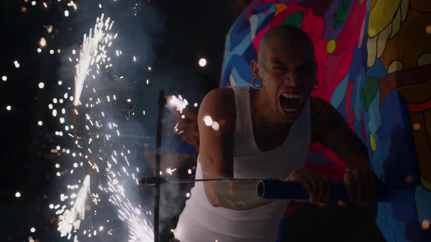 A man yells intensely as he runs and pushes a large parade float with rotating sparklers shooting sparks everywhere