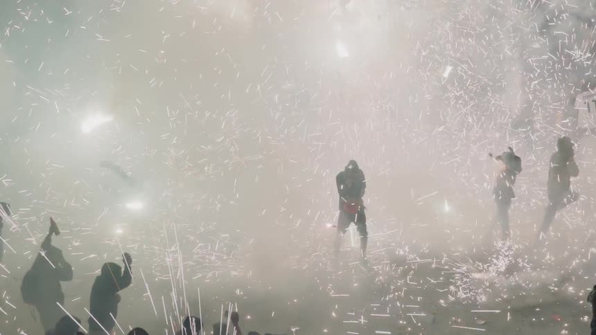 A large crowd of people stand amidst an enormous cloud of sparkling fireworks and smoke