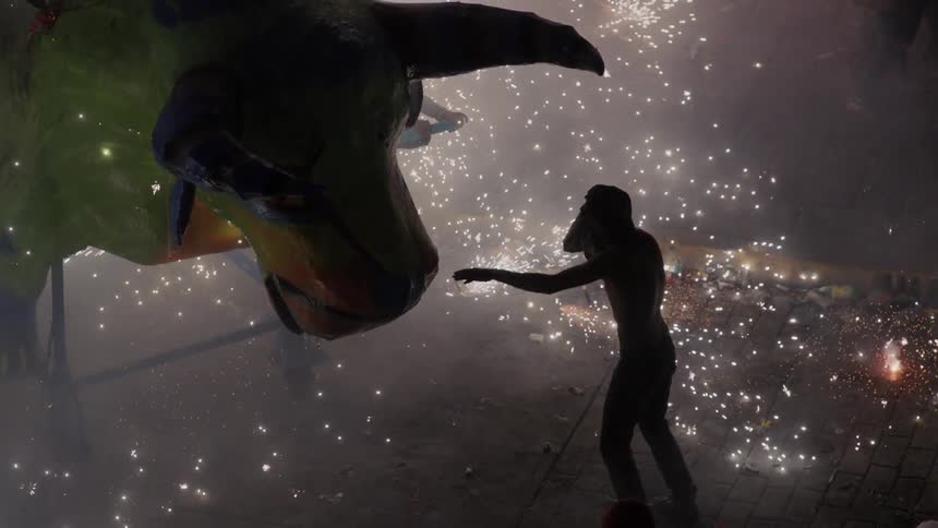 Men interact with bull model among shooting fireworks