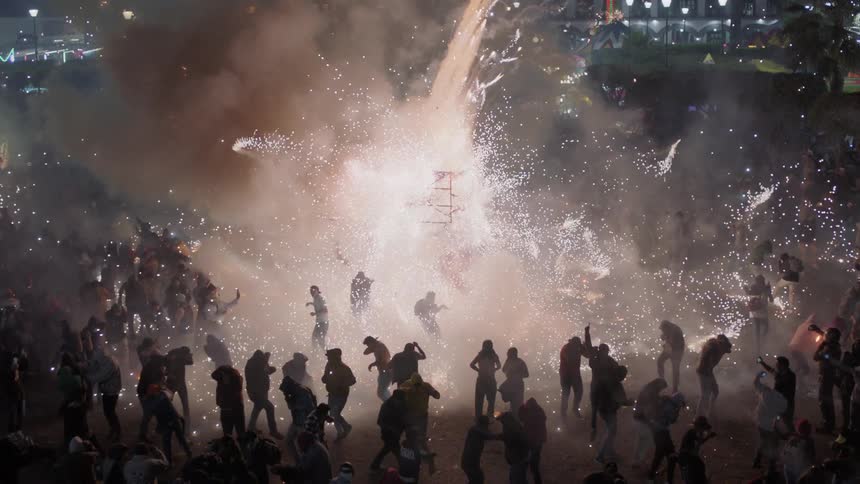 Crowd celebrates outdoors as fireworks display fires off at the center
