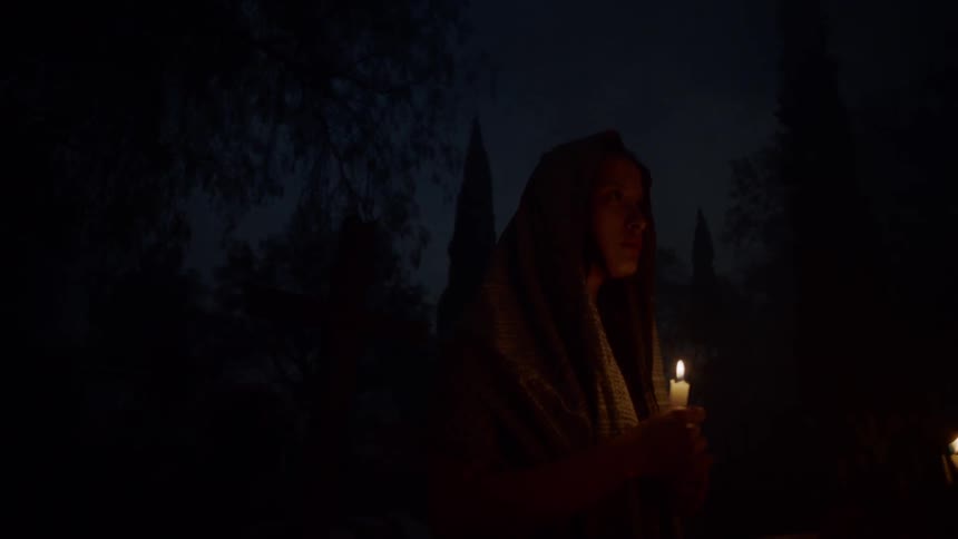 A woman stands in the dark holding a candle
