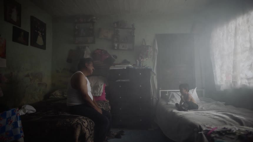 An older hispanic male sits in a bedroom and talks to a small boy on the adjacent bed