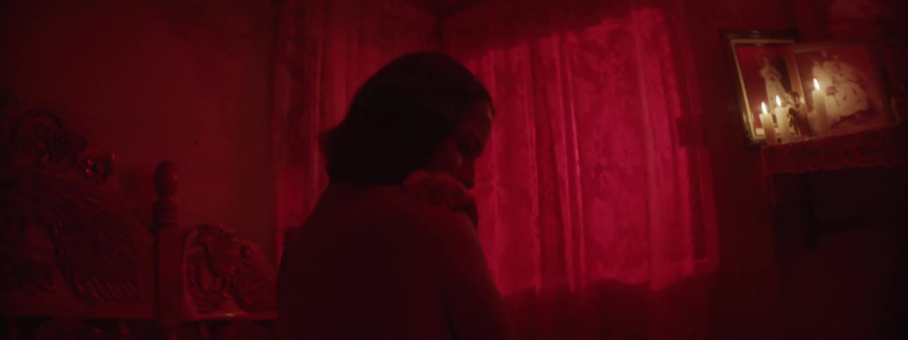 A young woman hugs herself in a dark room