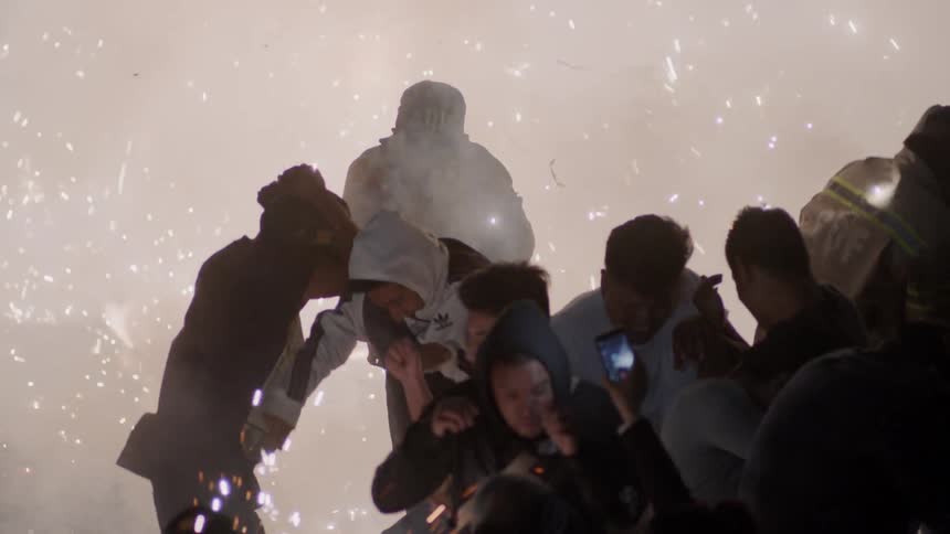 A group of teens dance and jump as sparks fly in a smoke filled area