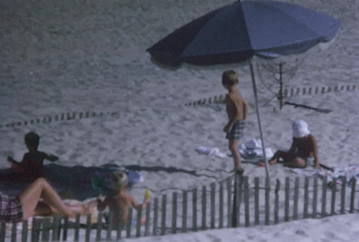 People are sitting on the sand of a beach some children are playing