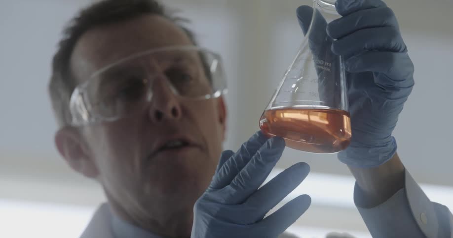 Man wearing safety glasses and gloves examines the liquid in a beaker