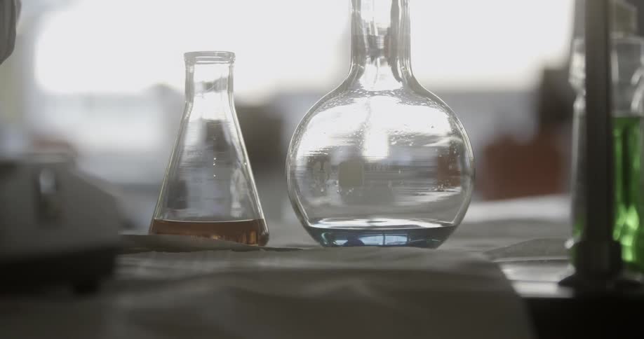Beakers full of liquid sit on a table in front of a window