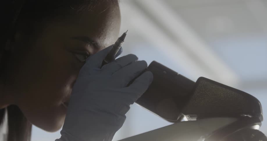 Teenage girl wearing gloves looking at a microscope