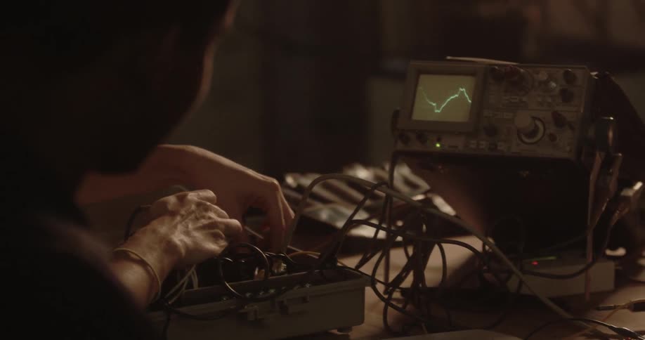 Two people work together to make adjustments to equipment that is connected to an oscilloscope