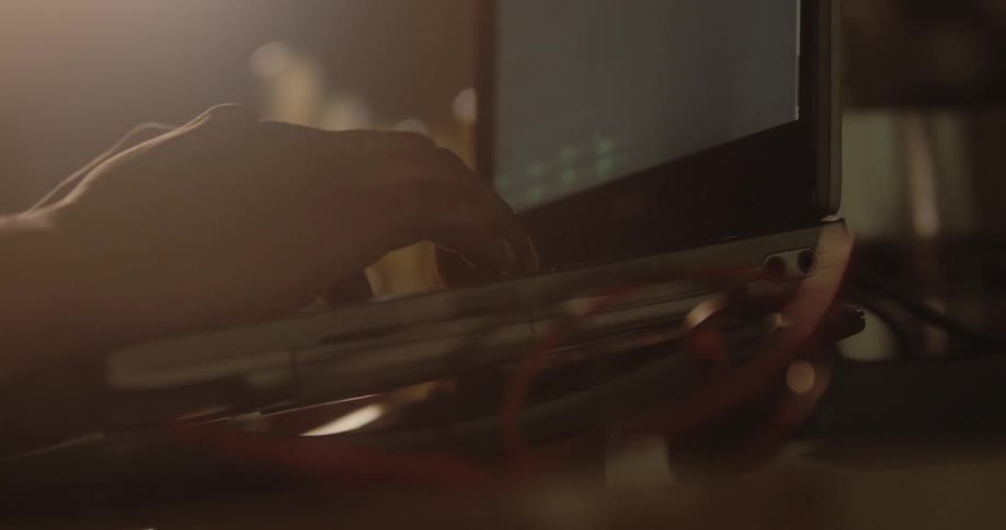 A person is typing on the keyboard of a compact laptop in a dimly light room