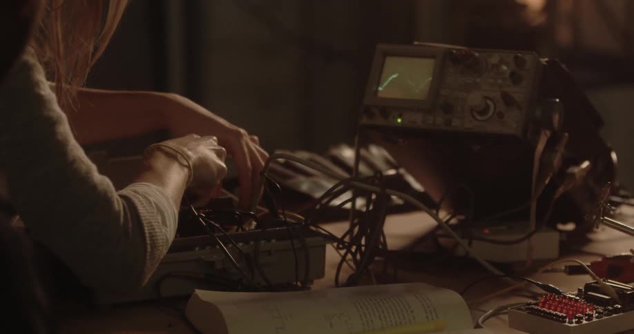 A woman is working on some electronics with an electrical signal shown on a screen