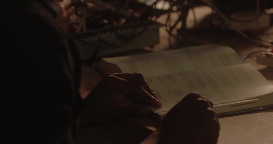 A boy reads a book at a desk while a girl works with some electronics