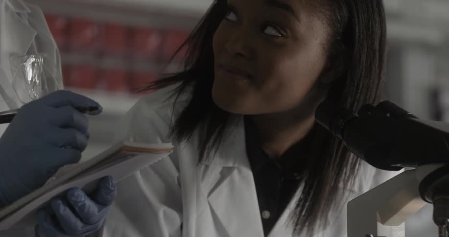 A woman looks in a microscope then looks up and smiles