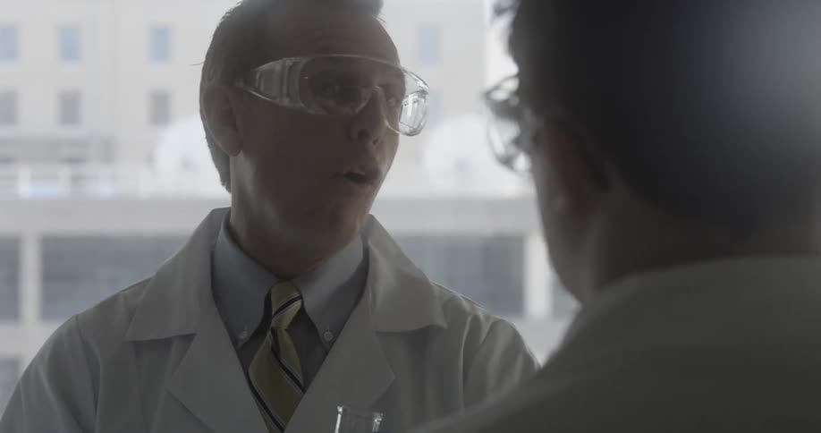 Men wearing white coats and holding beakers talk to each other