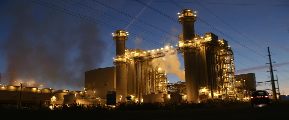 Cars drive by a lit up factory at night