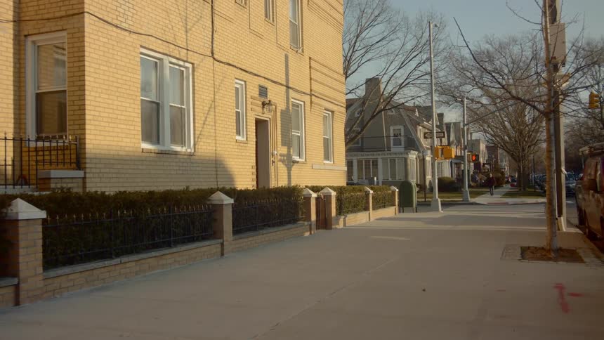 Cars travel on a cross street in a neighborhood with large empty sidewalks