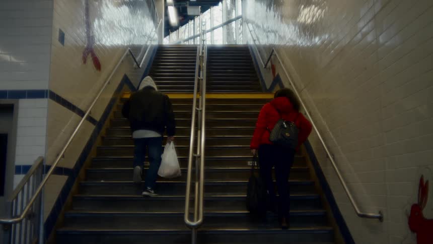 Two people climb a long flight of stairs toward brightly lit ground level