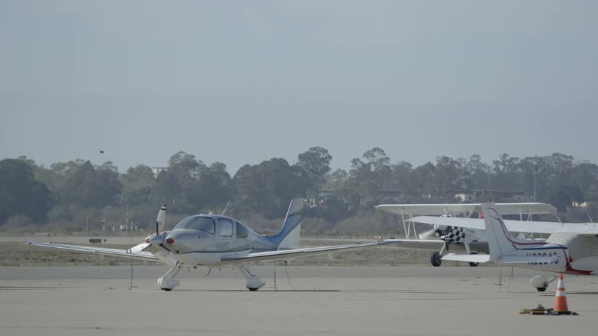 Biplane taxiing past other non-moving planes on a clear day