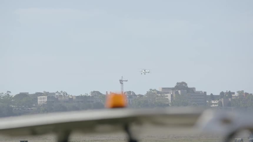A bi-plane soars above buildings and an airfield during the day