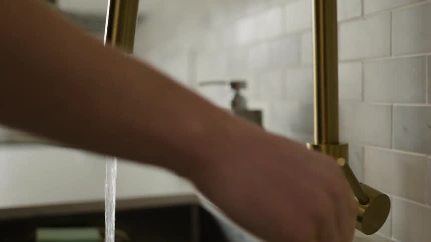 A woman turns on a faucet and puts soap in her hands