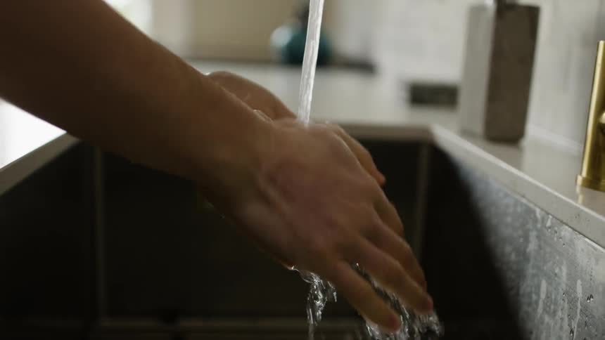 A woman washes her hands over a kitchen sink