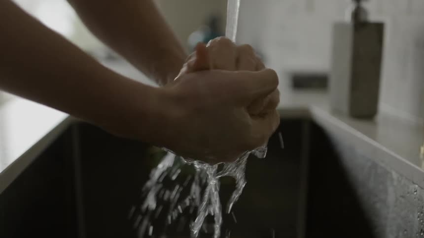 A woman washes her hands in a sink and rubs her hands together under flowing water