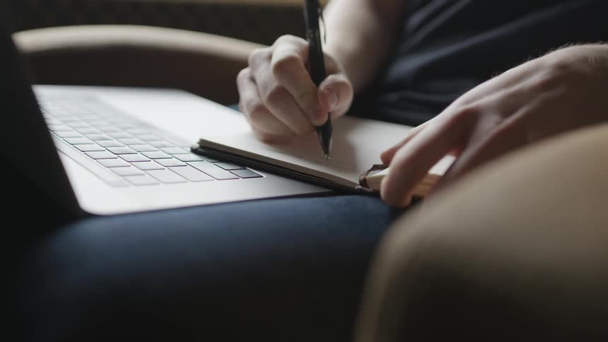 Person takes notes on notepad while using laptop