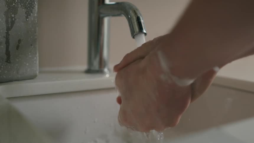 A person washes their hands with soap under running water at the bathroom sink
