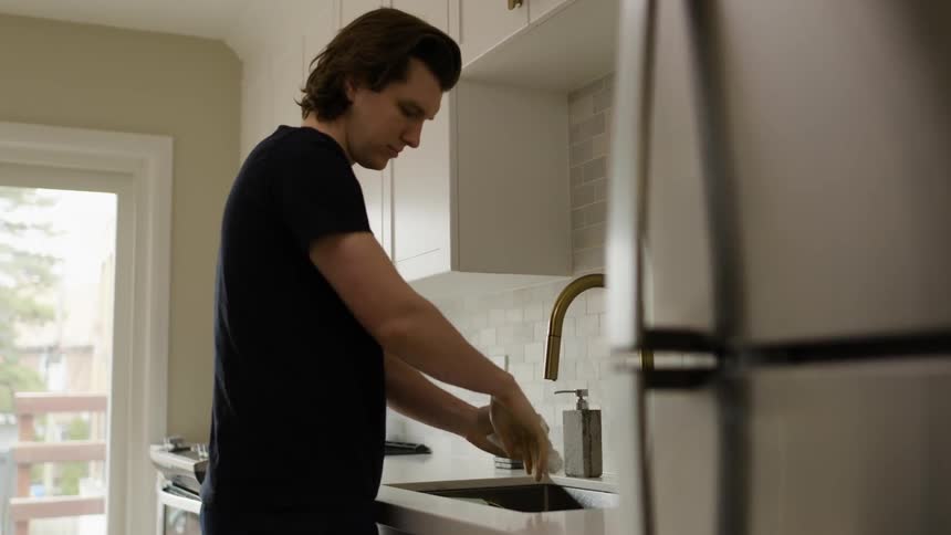 Man drys hands and wrists near kitchen sink