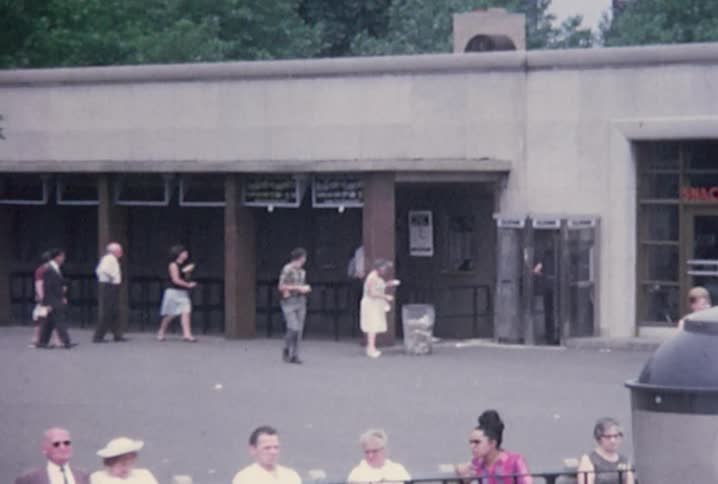 People are walking in and out of a building and some are sitting on benches