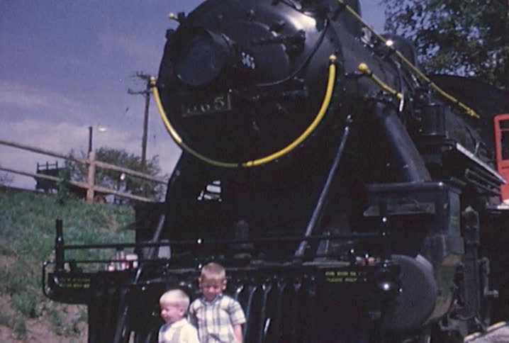 Old footage of two little boys standing in front of a train engine