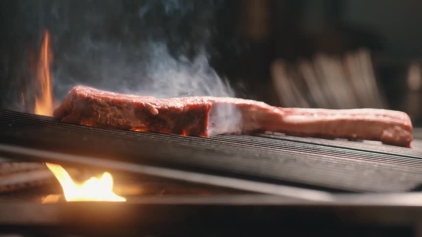 A steak is cooked on a grill above an open flame