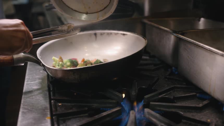Vegetables are poured into a pan on hot gas stove