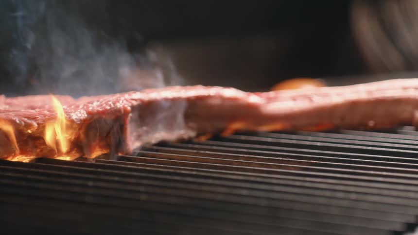 Smoke rises from a steak being cooked on a grill