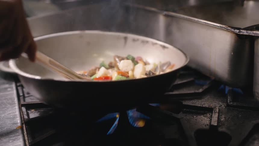 A cook stirs ingredients in a pan