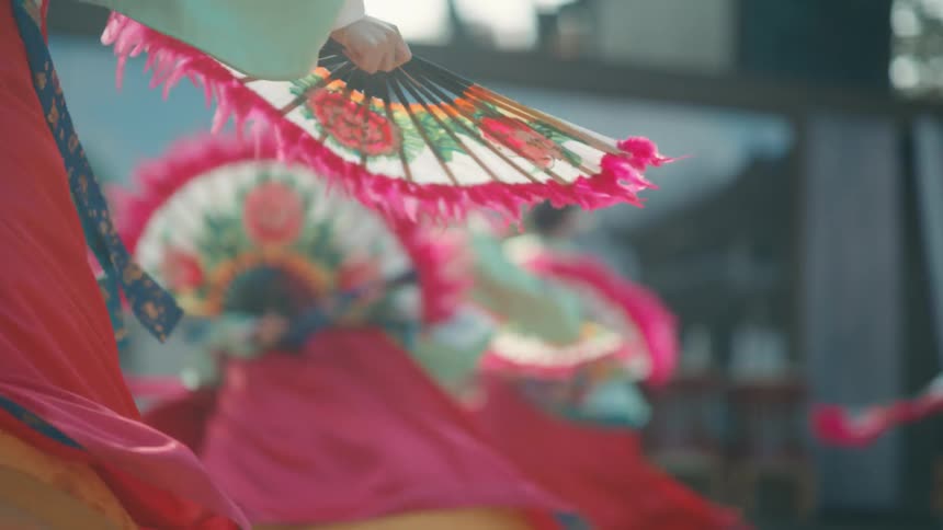 Women perform a traditional asian dance outdoors in full costume and with fans
