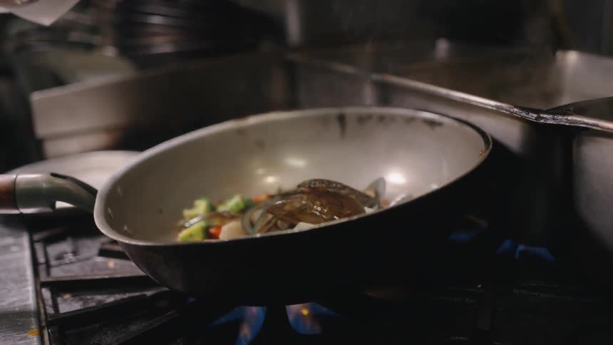 A cook pouring food from a frying basket into a skillet