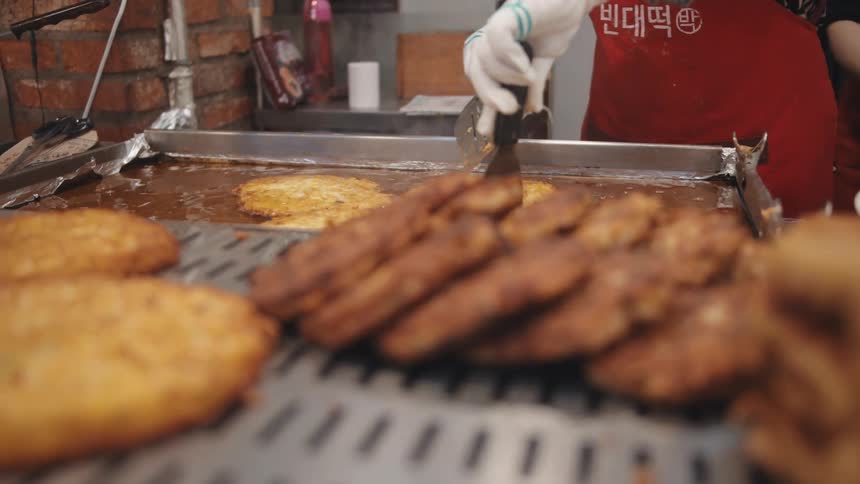 A korean cook frying food while wearing a red apron