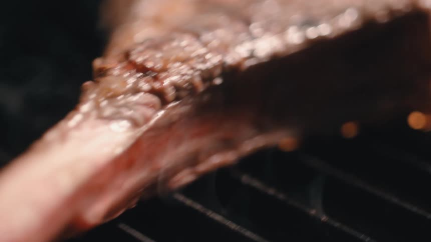 Smoke rises up through the grill grate where a chop is cooking