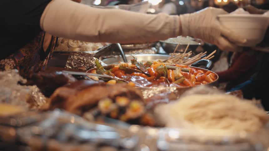 A word unwrapping and handing a bowl of food to a person on the opposite side of a long table of food
